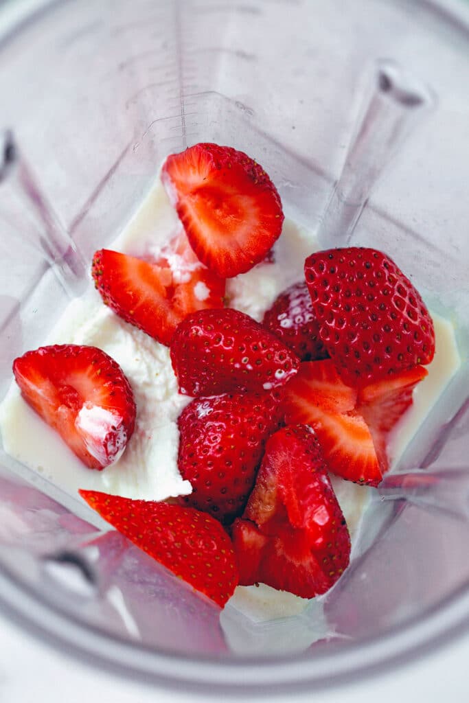 Overhead view of yogurt, coconut milk, and strawberries in blender