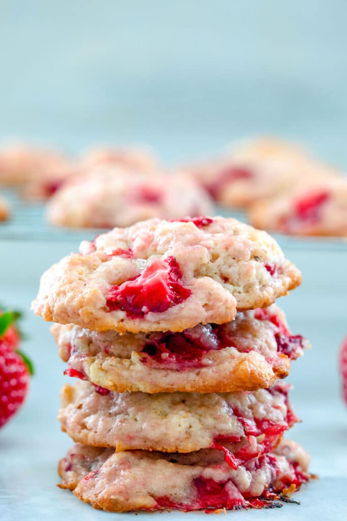 Head-on closeup view of four strawberry shortcake cookies stacked on top of each other with more cookies in background.