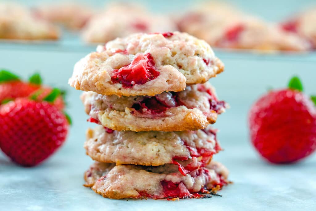 Landscape head-on view of stack of strawberry shortcake cookies with whole strawberries all around.