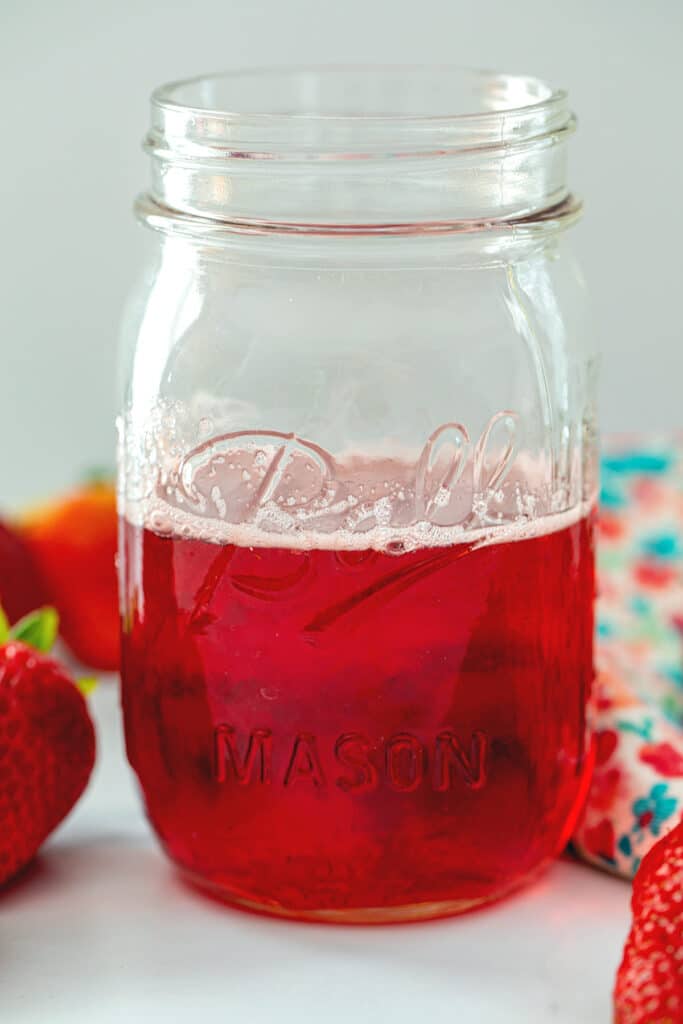Closeup head-on view of a mason jar of strawberry simple syrup.