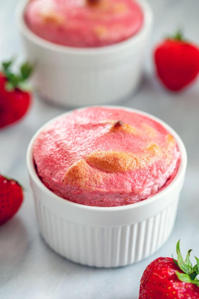 Closeup overhead view of a pink strawberry souffle in white ramekin with strawberries and another souffle in background