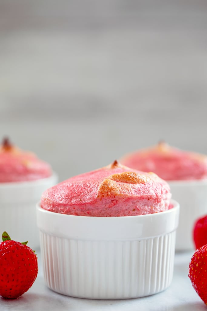 Head-on closeup view of a pink strawberry souffle in a white ramekin