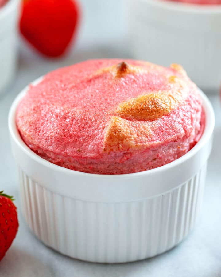 Head-on view of strawberry souffle in white ramekin with strawberries all around