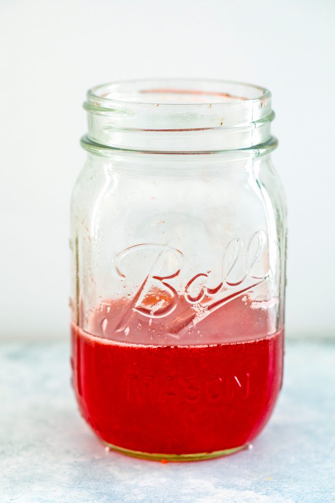 Head-on view of a mason jar filled with red homemade strawberry syrup
