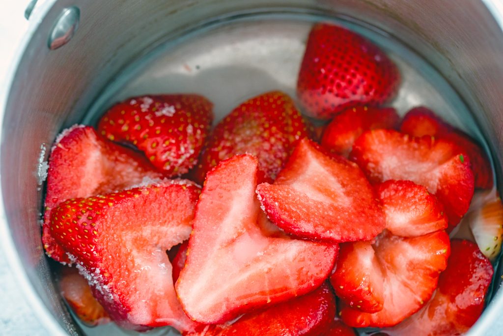 Overhead view of strawberries, sugar, and water in a saucepan