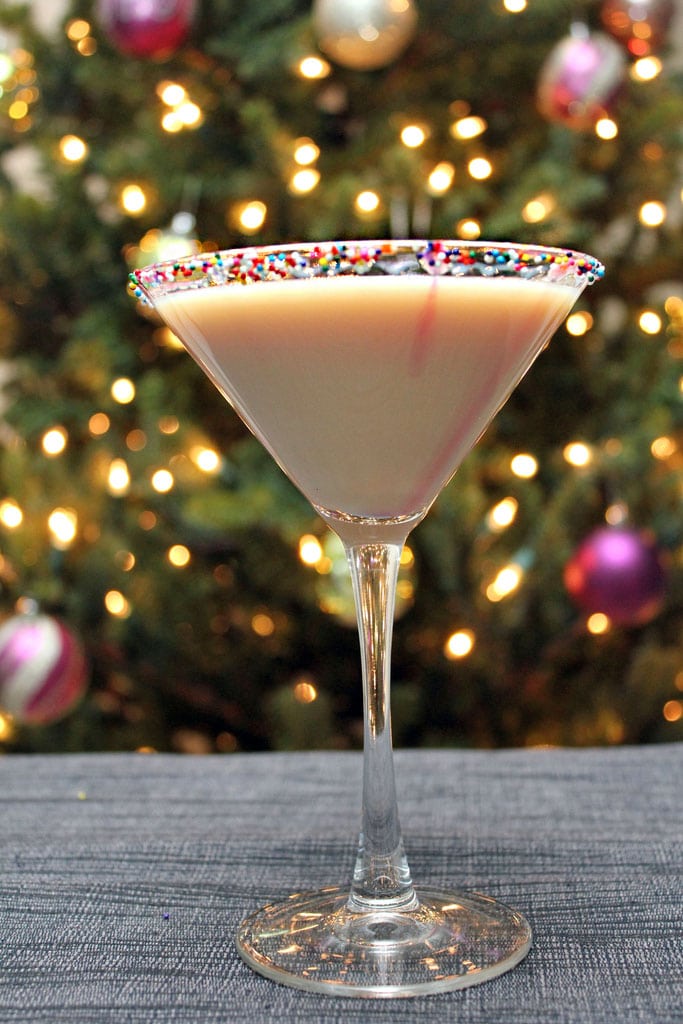 Head-on view of a sugar cookie martini with sprinkles rim in front of a lit Christmas tree