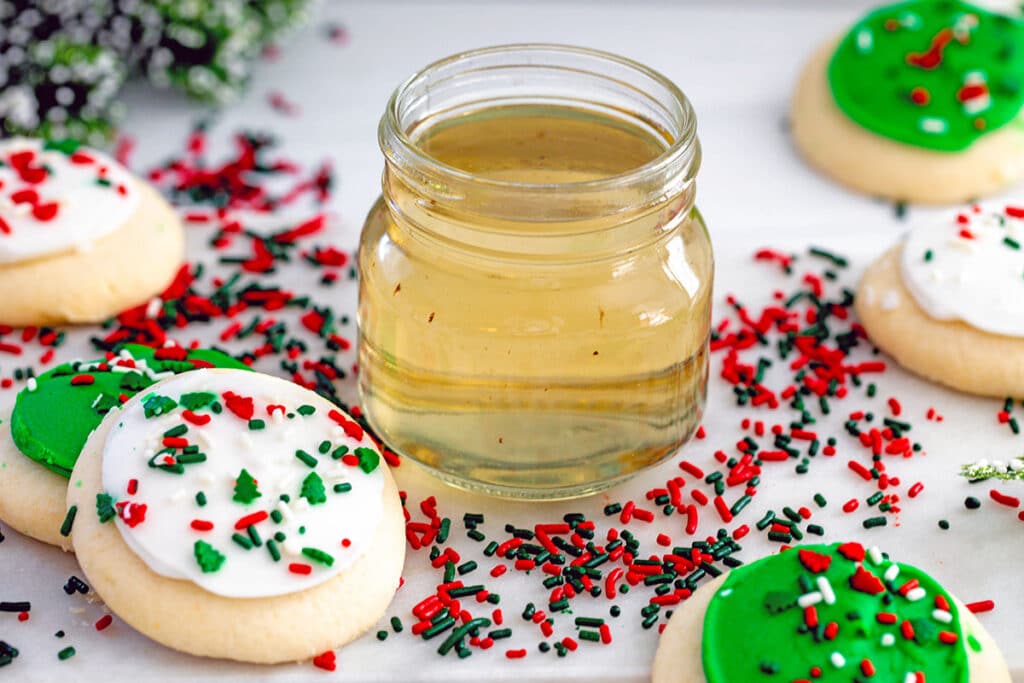 Landscape overhead photo of sugar cookie syrup in small jar with red and green sprinkles and Christmas cookies all around.