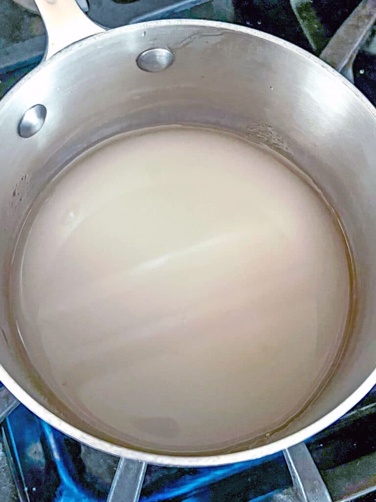 Overhead view of sugar and water in saucepan.