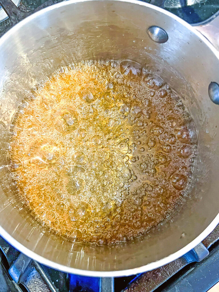 Sugar and water simmering and starting to turn golden from caramelizing in saucepan.