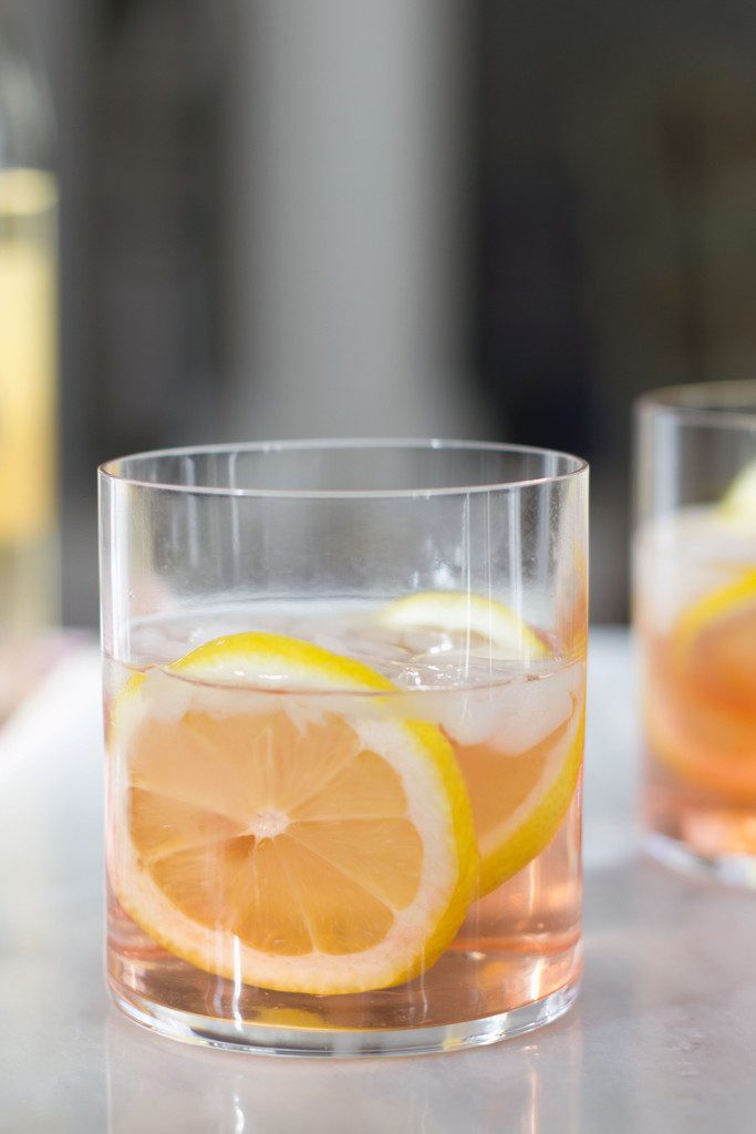 A head-on view of a pink rosé spritzer in a rocks glass with lemon rounds on a white marble surface