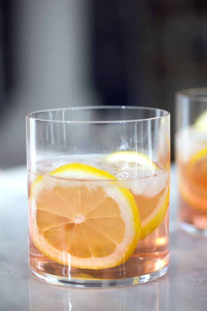 A head-on view of a pink rosé spritzer in a rocks glass with lemon rounds