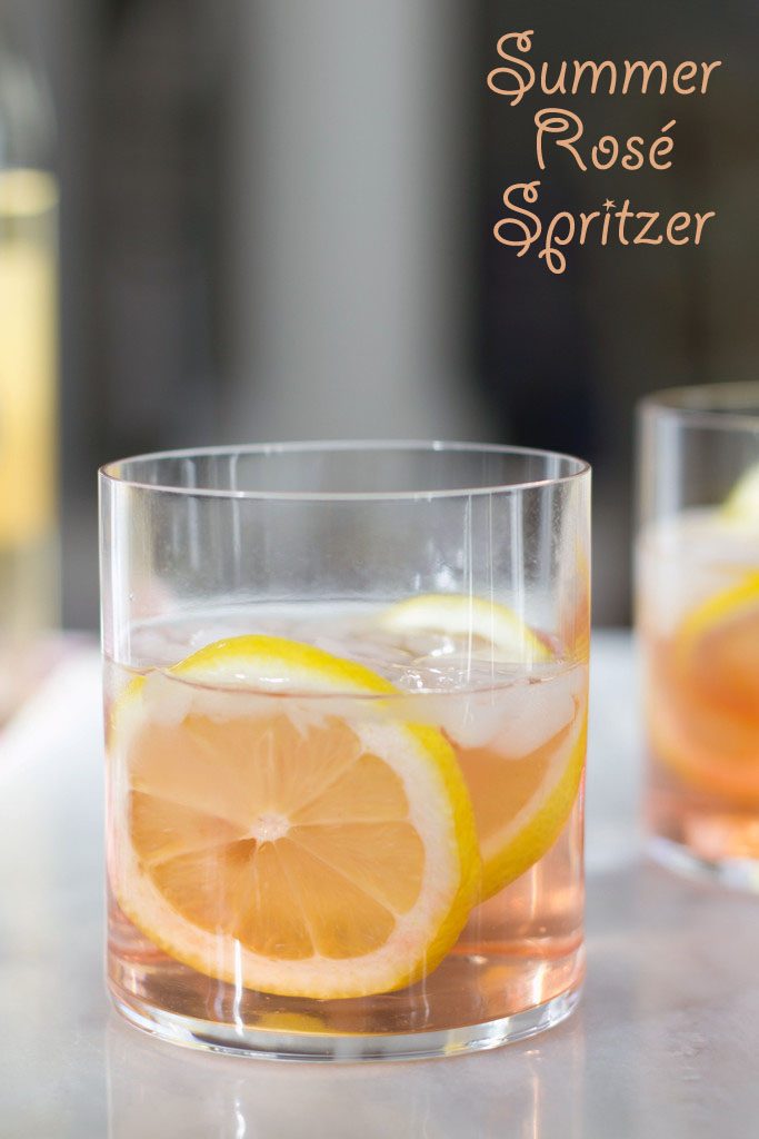 A head-on view of a pink rosé spritzer in a rocks glass with lemon rounds and "Summer Rosé Spritzer" text at top