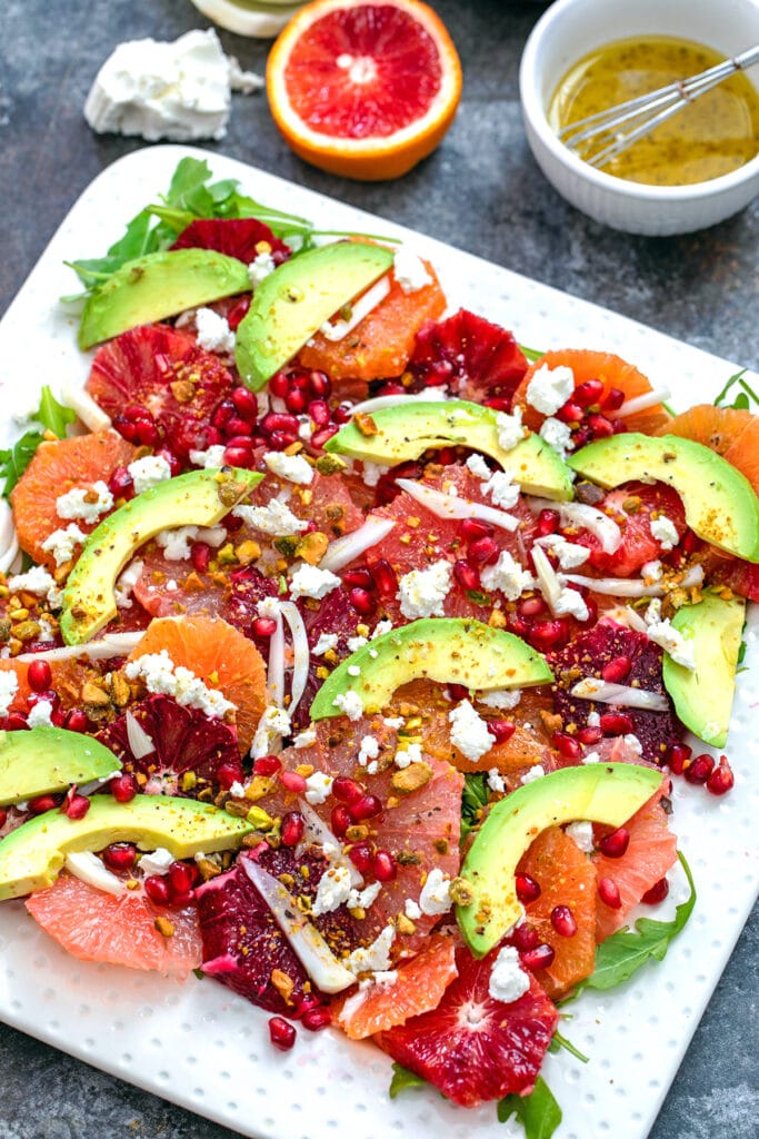 Overhead close-up view of winter citrus salad with blood oranges, cara cara oranges, grapefruit, fennel, avocado, goat cheese, and more with ingredients in the background