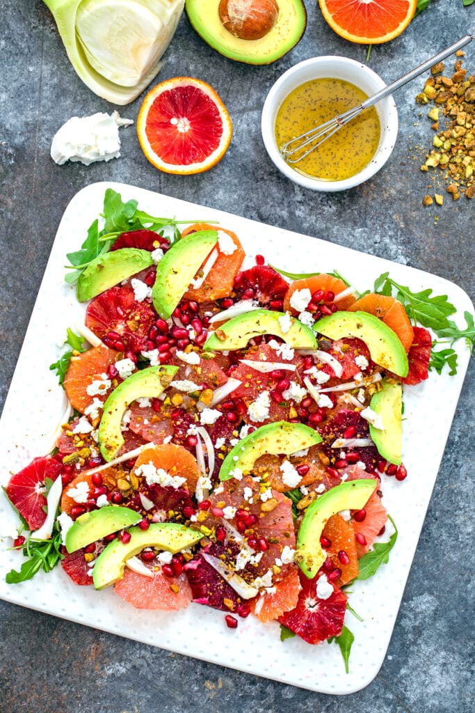 Bird's eye view of winter citrus salad with blood oranges, cara cara oranges, grapefruit, fennel, avocado, goat cheese, and more with some ingredients in the background