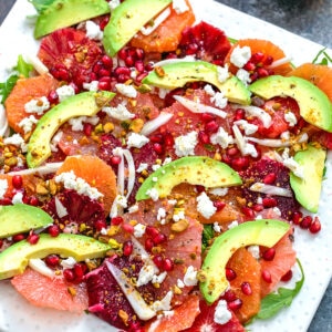 Close-up view of winter citrus salad featuring blood oranges, cara cara oranges, grapefruit, avocado, fennel, arugula, and goat cheese on white platter