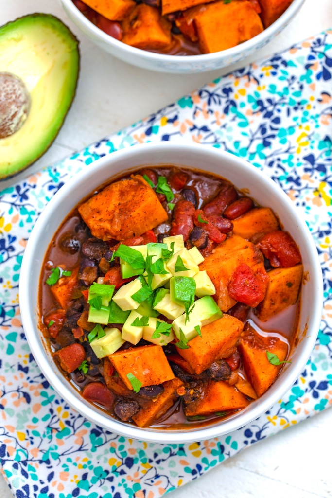 Overhead view of a bowl of sweet potato chili topped with avocado and cilantro with avocado in background