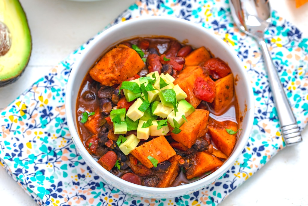 Overhead landscape view of sweet potato chili with avocado and cilantro garnish and spoon and avocado half in the background