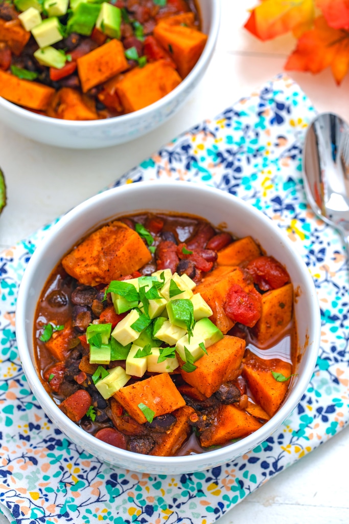 Overhead view of sweet potato chili with avocado and cilantro garnish with spoon and second bowl of chili in the background