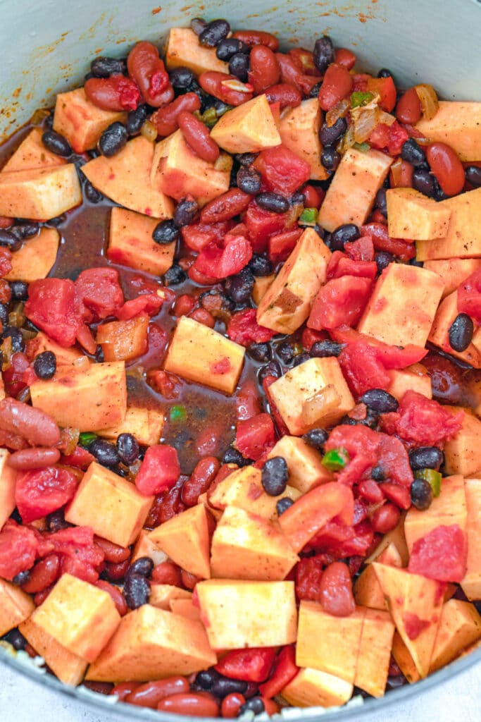 Overhead view of with sweet potatoes, black beans, kidney beans, and tomatoes cooking in dutch oven