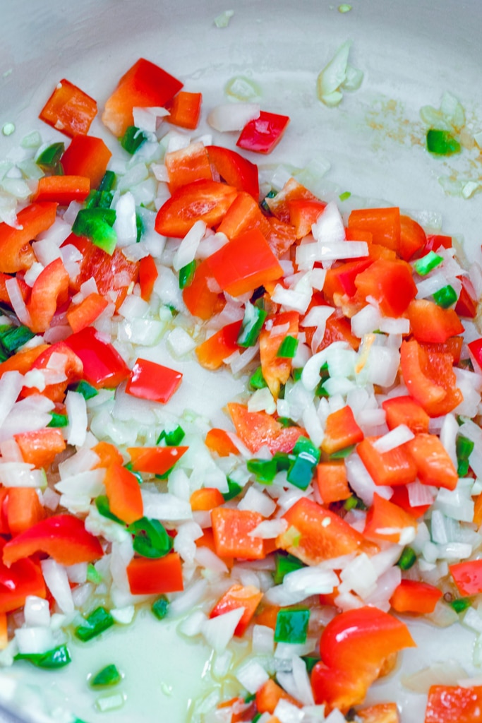 Overhead view of red pepper, jalapeño, onion, and garlic cooking in olive oil in a dutch oven