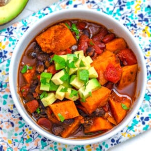 Overhead view of a bowl of sweet potato chili topped with avocado and cilantro with avocado in background
