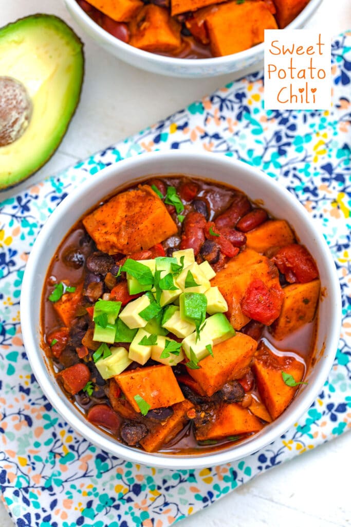 Overhead view of a bowl of sweet potato chili topped with avocado and cilantro with avocado in background and recipe title at top
