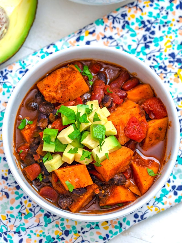 Overhead closeup view of a bowl of sweet potato chili topped with avocado and cilantro with avocado in background