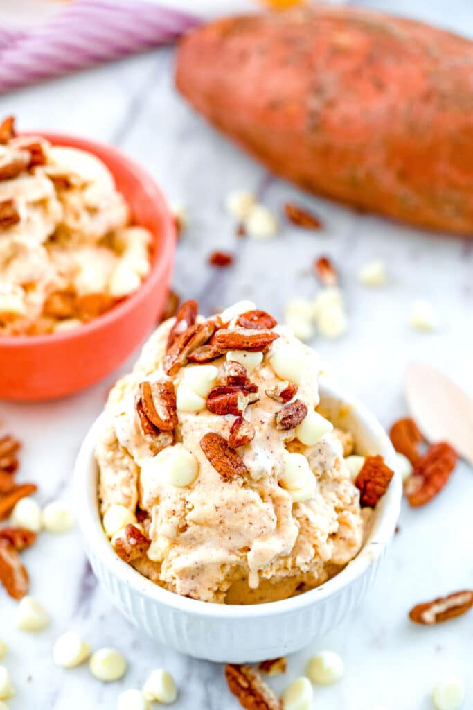 Overhead view of sweet potato ice cream topped with toasted pecans and white chocolate chips with whole sweet potato in the background