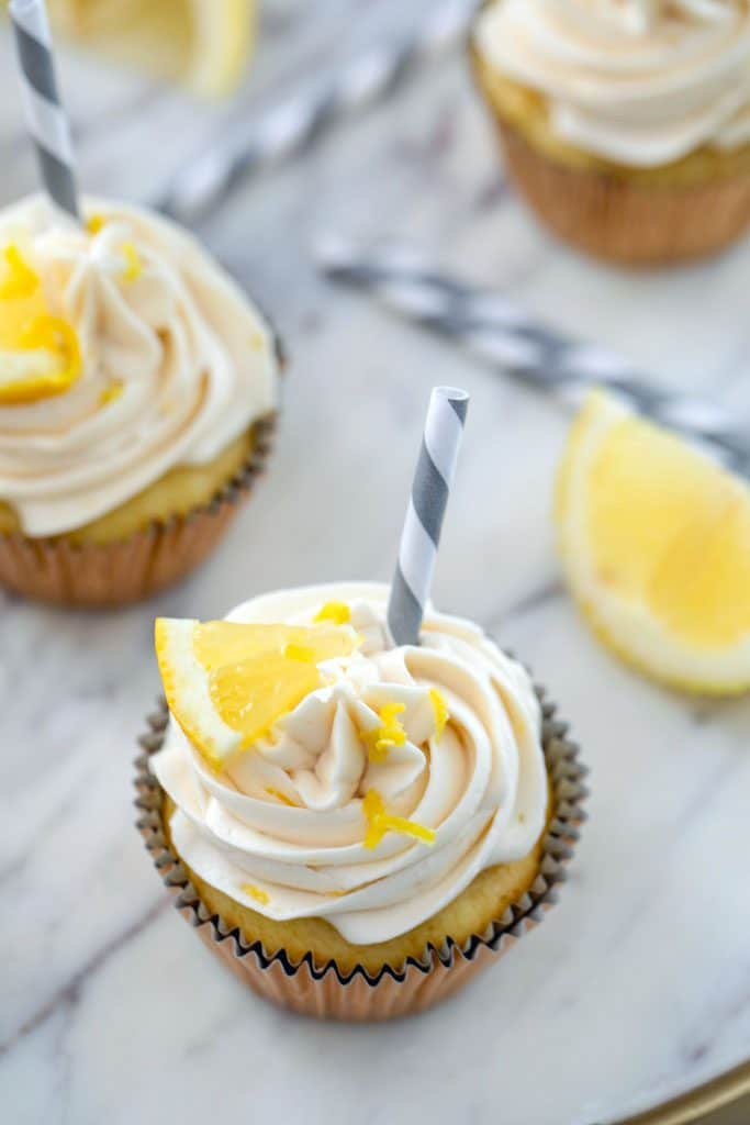 Bird's eye view of multiple sweet tea vodka cupcakes with grey and white striped straws, lemon wedges, and lemon zest on a marble surface