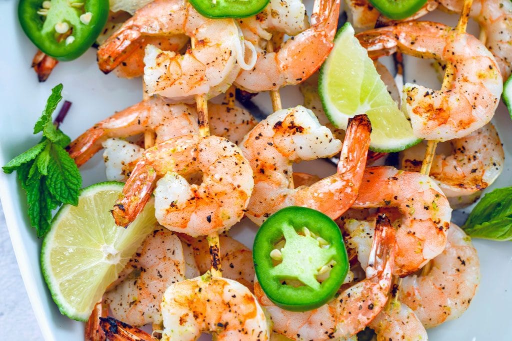 Paisagem foto que mostra o close-up de cozido tequila espetos de camarão com pimenta jalapeño rodelas, fatias de limão e folhas de hortelã