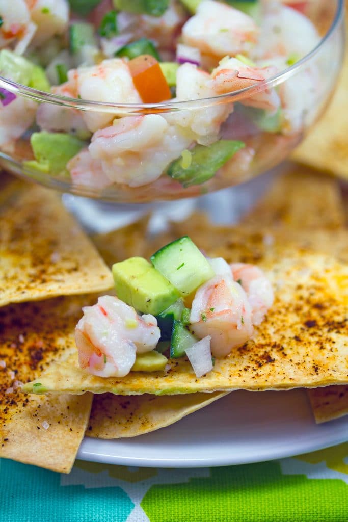 Head-on view of chile dusted tortilla chips on a plate topped with tequila shrimp ceviche with bowl of ceviche in background