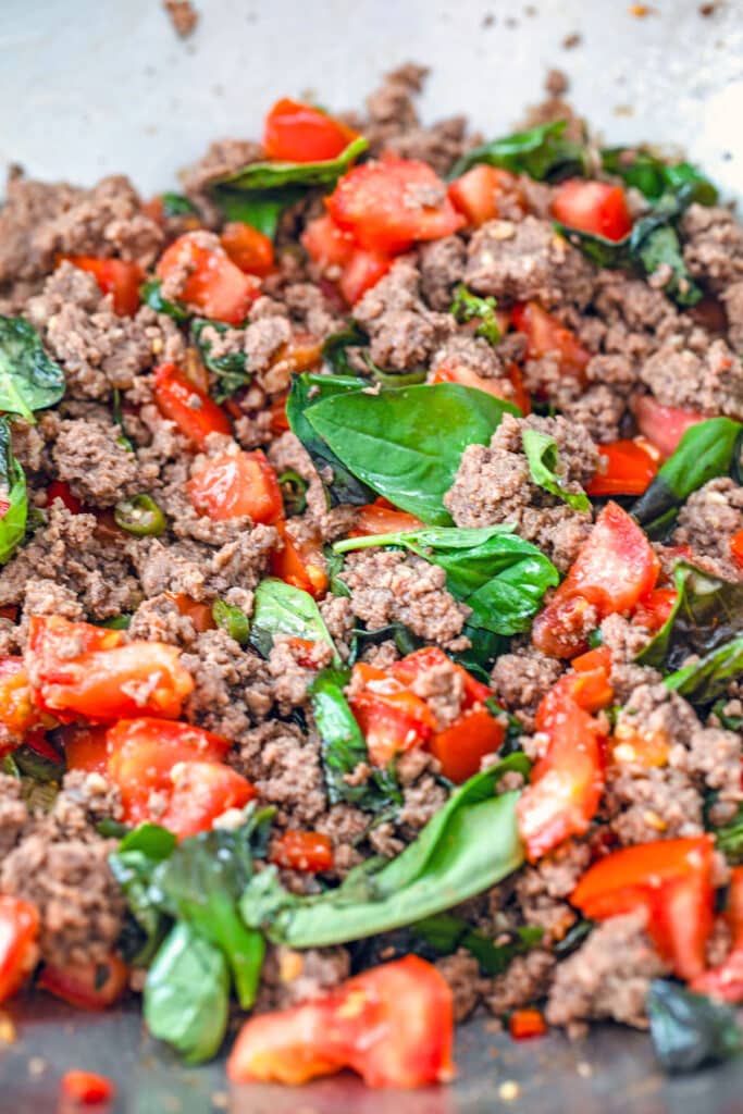 Ground beef in wok with basil, tomatoes, and npeppers.