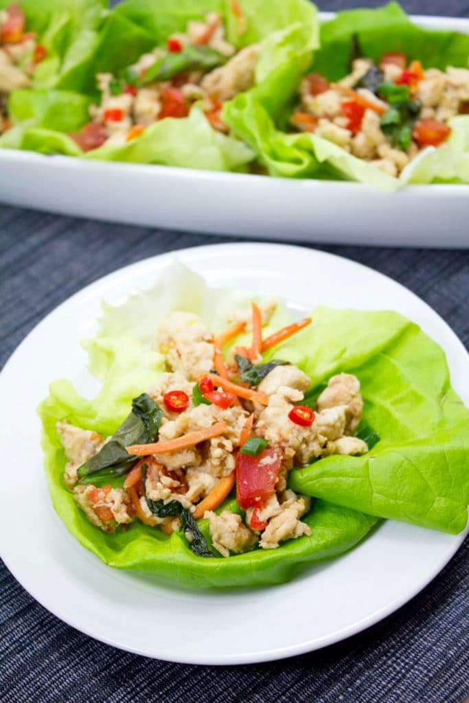 Overhead view of a white plate with a Thai chicken basil lettuce wrap on it, with more lettuce wraps on a platter in the background
