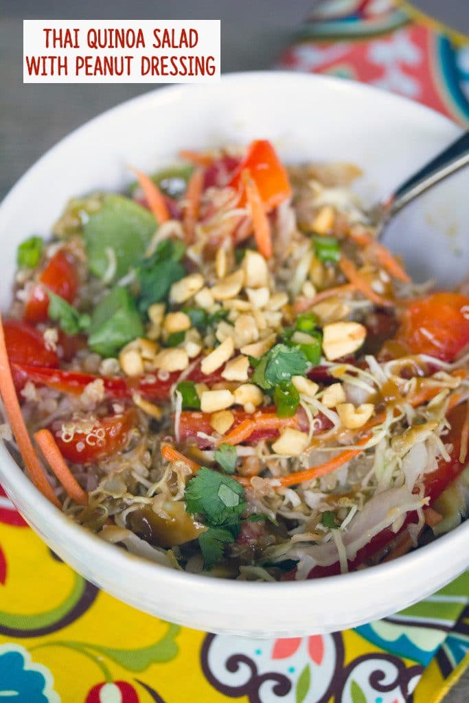 Overhead view of Thai quinoa salad with peanut dressing in a white bowl on a colorful napkin with recipe title at top