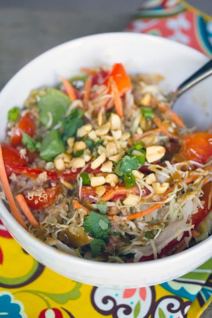 Overhead view of Thai quinoa salad with peanut dressing in a white bowl on a colorful napkin