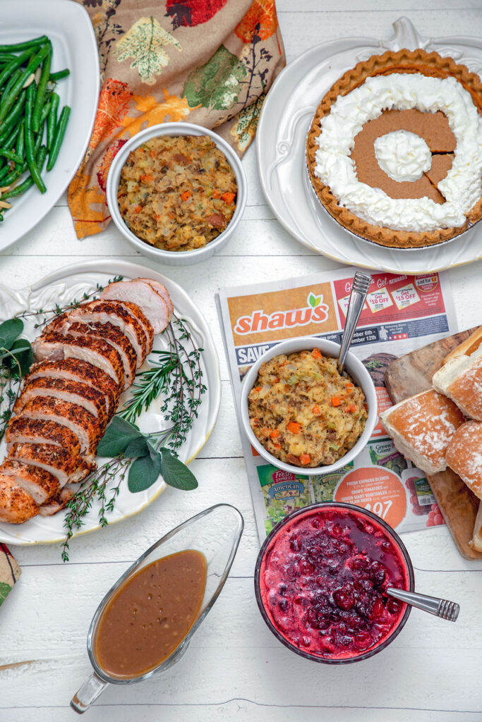 Overhead view of full Thanksgiving dinner, including turkey breast, stuffing, cranberry sauce, rolls, pumpkin pie, and gravy.