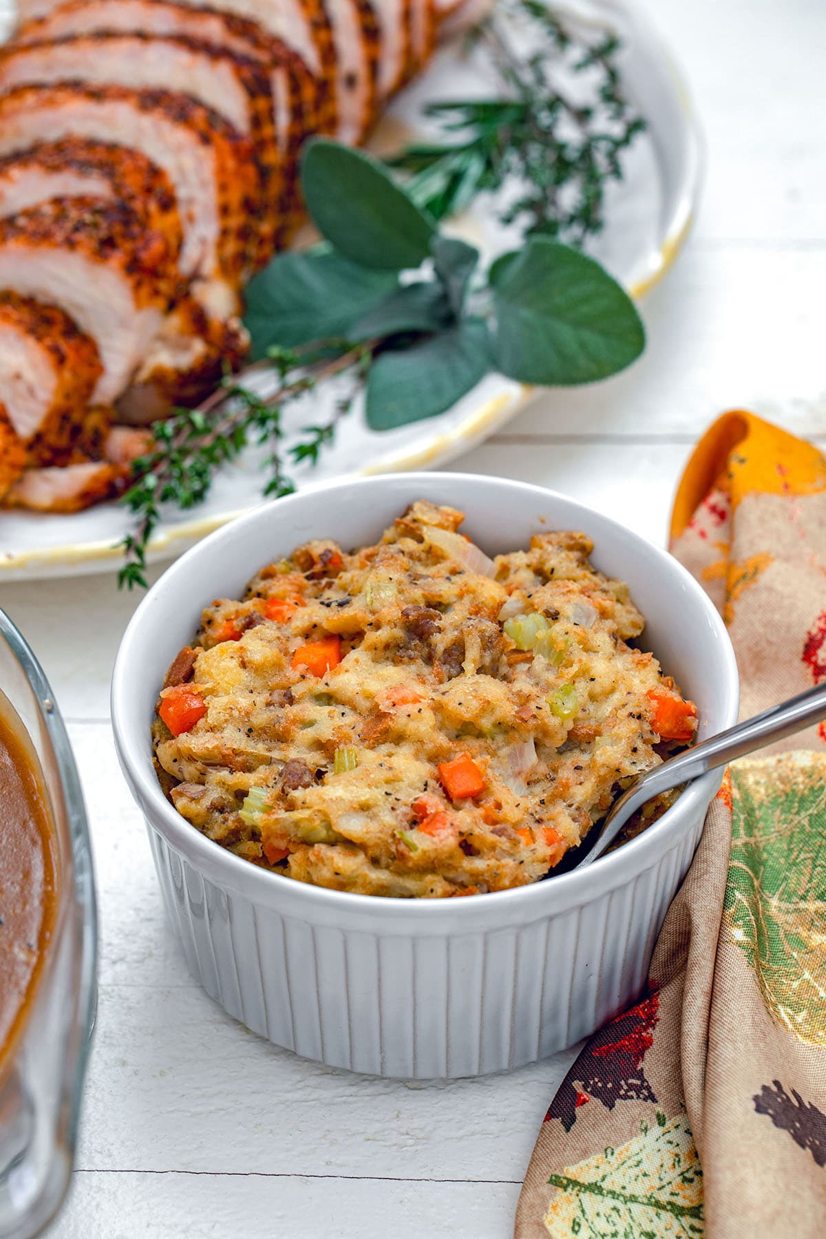 Head-on view of Thanksgiving stuffing in small casserole dish with turkey platter in background.