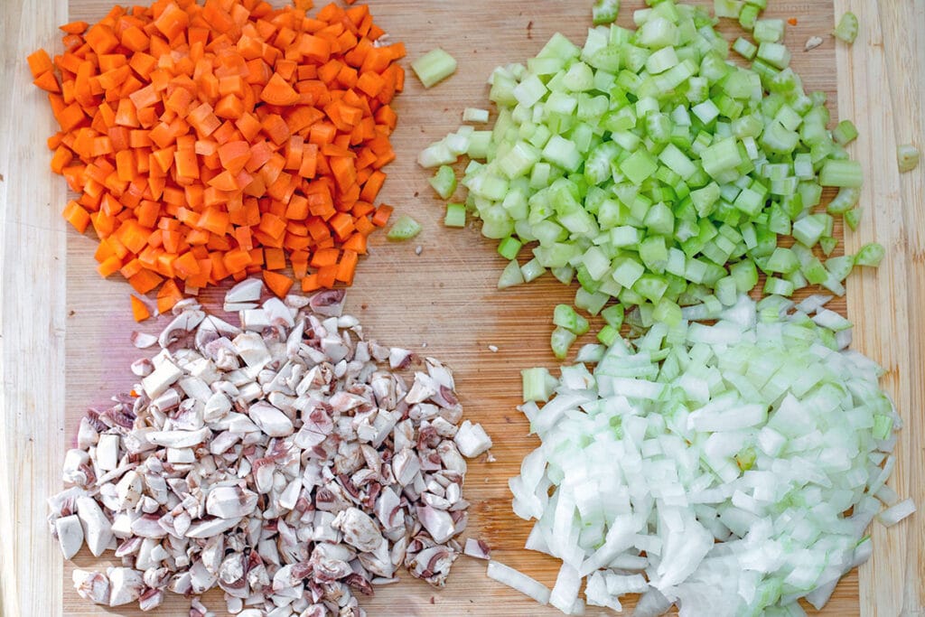 Cutting board with diced carrots, celery, mushrooms, and onions.