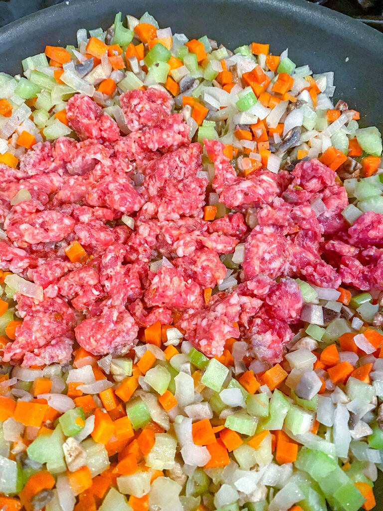 Vegetables cooking in a skillet with sausage.