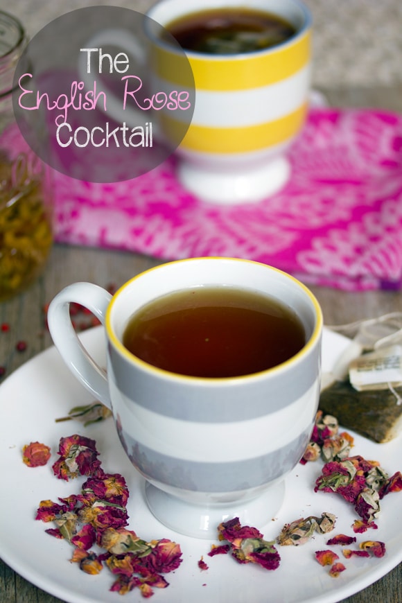 Head-on photo of two striped teacups filled with English Rose cocktail with one on a white plate, surrounded by dried roses and a tea bag with "English Rose Cocktail" text at top