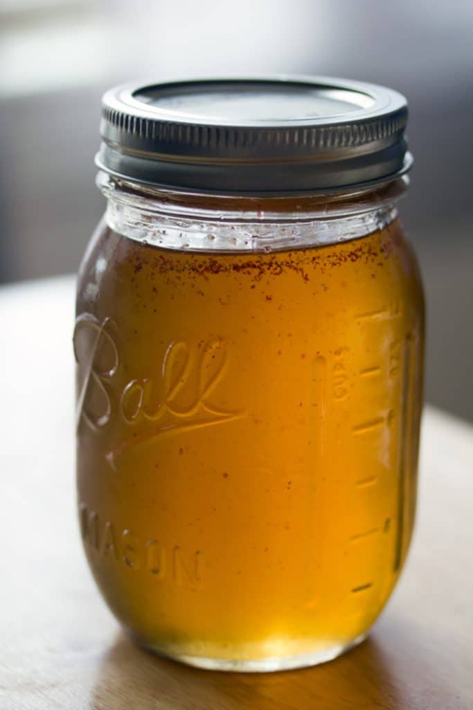 Head-on view of pink peppercorn simple syrup in a mason jar