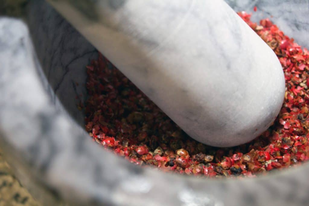 Pink peppercorns being crushed with a mortar and pestle