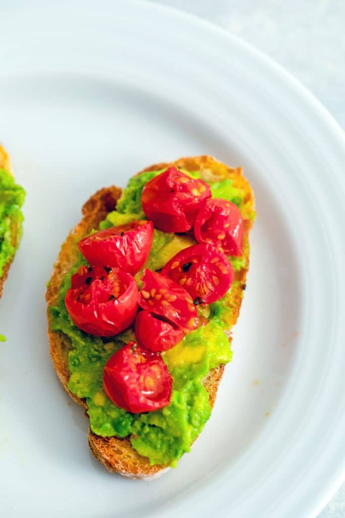 Overhead view of piece of toast spread with mashed avocado and topped with roasted tomatoes