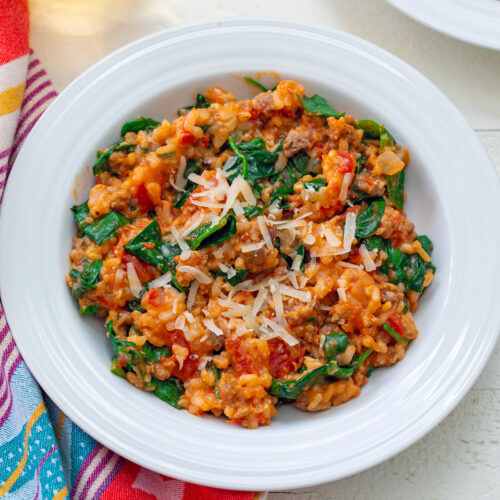 Overhead closeup view of a bowl of tomato and sausage risotto with spinach mixed in and parmesan cheese on top