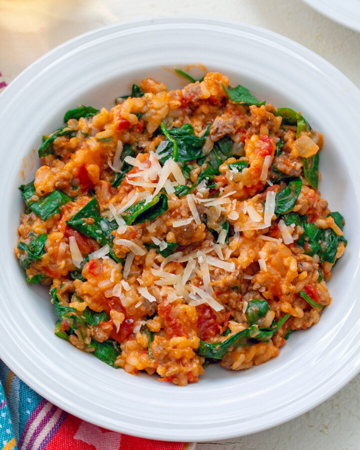 Overhead closeup view of a bowl of tomato and sausage risotto with spinach mixed in and parmesan cheese on top