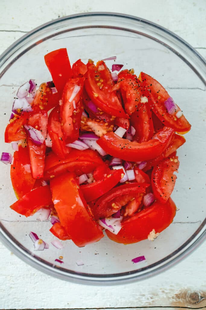 Overhead view of tomatoes, red onion, and garlic in a bowl