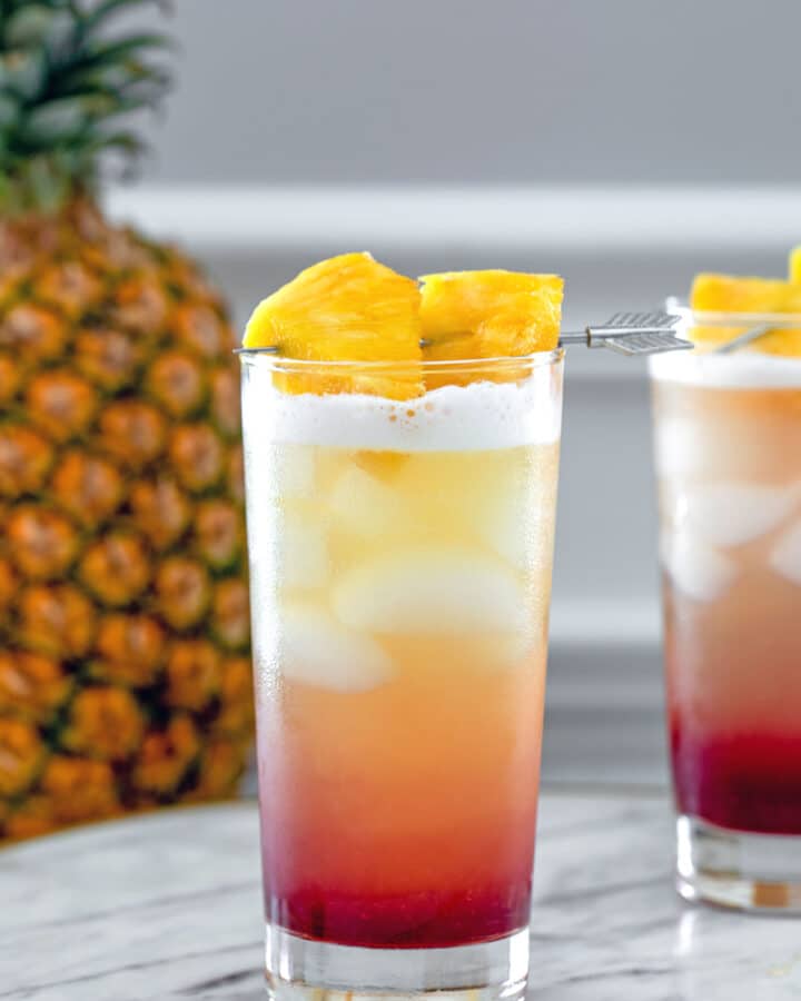 Tropical Gin Sunrise -- Tropical Gin Sunrise cocktails are a visually stunning combination of pineapple juice, gin, raspberry lambic and lemon juice. They're easy to mix and perfect for summer sipping! | wearenotmartha.com #gin #cocktails #tropicaldrinks #gindrinks