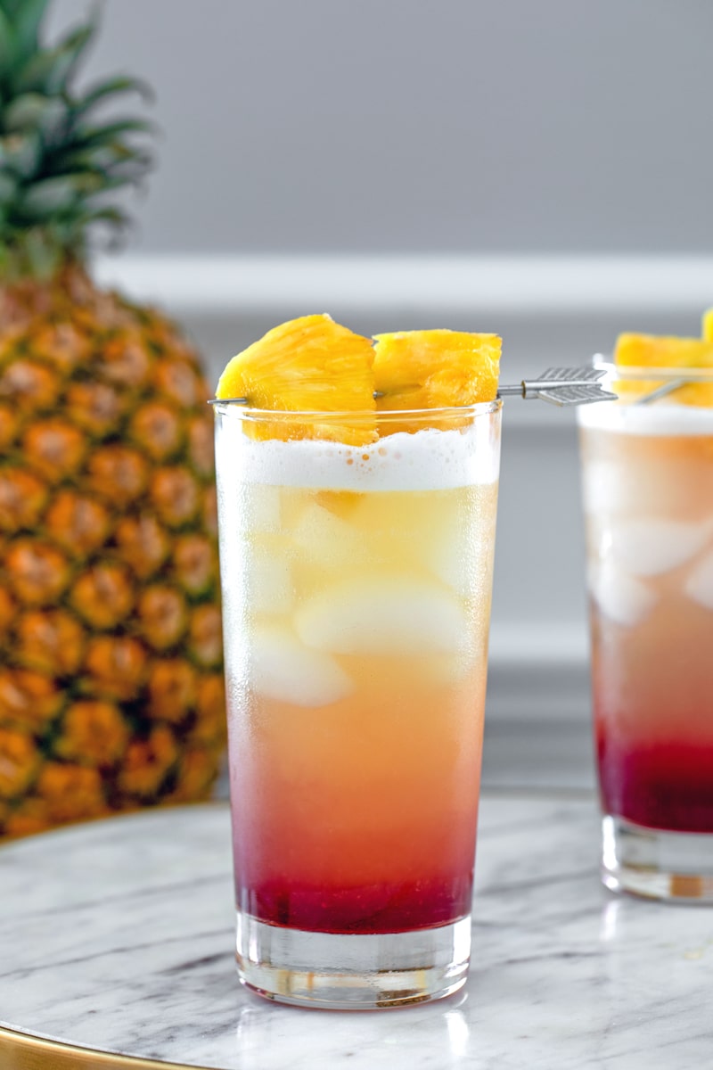 Tropical Gin Sunrise -- Tropical Gin Sunrise cocktails are a visually stunning combination of pineapple juice, gin, raspberry lambic and lemon juice. They're easy to mix and perfect for summer sipping! | wearenotmartha.com #gin #cocktails #tropicaldrinks #gindrinks