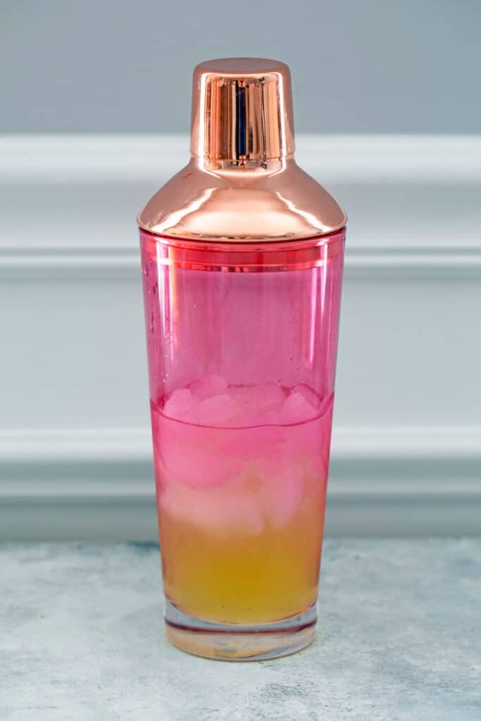 Head-on view of pink glass shaker with pineapple juice, lime juice, and gin in it