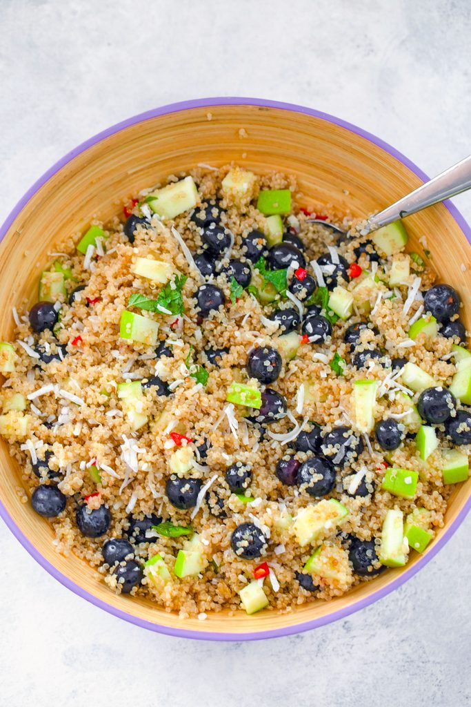 Overhead view of tropical quinoa salad with blueberries, chopped green apple, shredded coconut, chopped mint, and red chili peppers all tossed together